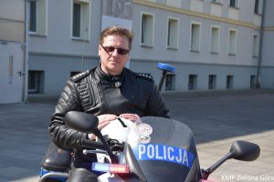zdjęcie kolorowe, policjant w okularach przeciwsłonecznych siedzący na policyjnym motocyklu