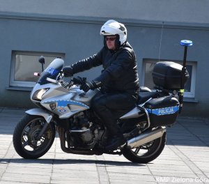 zdjęcie kolorowe, policjant w białym kasku motocyklowym jadący na policyjnym motocyklu na tle ściany budynku