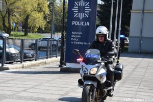 zdjęcie kolorowe, policjant w białym kasku motocyklowym siedzący na policyjnym motocyklu obok granatowego pylonu z napisem Komenda Miejska Policji w Zielonej Górze