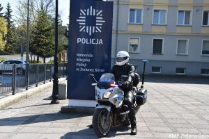 zdjęcie kolorowe, policjant w białym kasku motocyklowym siedzący na policyjnym motocyklu obok granatowego pylonu z napisem Komenda Miejska Policji w Zielonej Górze