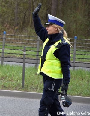 fotografia kolorowa, policjantka ruchu drogowego z uniesioną ręką zatrzymuje pojazd na drodze