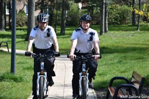 zdjęcie kolorowe, dwaj policjanci w patrolu rowerowym  jadą alejką w parku, widok z przodu