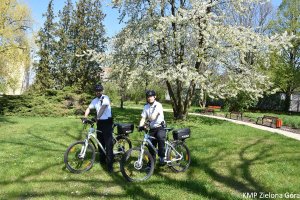 zdjęcie kolorowe, dwaj policjanci w patrolu rowerowym  stoją przy rowerach w parku