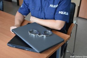 Policjant siedzący nad kajdankami położonymi na laptopie