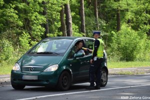 Zdjęcie policjanta sprawdzającego alkomatem trzeźwość kierowcy siedzącego w zielonym aucie
