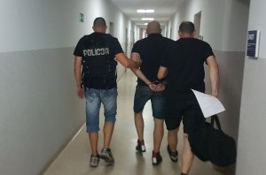 Dwóch policjantów prowadzących mężczyznę zakutego w kajdanki przez korytarz
