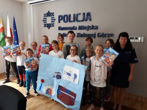 Grupa dzieci trzymających własnoręcznie zrobiony plakat stojących z uśmiechniętą policjantką