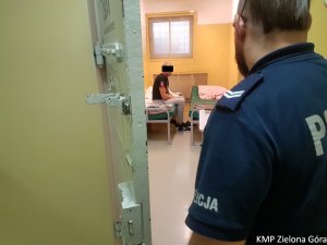 Mężczyzna siedzący w policyjnym areszcie i patrzący na niego przez otwarte drzwi policjant