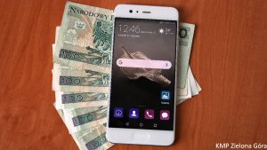 Biały telefon komórkowy leży na banknotach o nominale 100zł