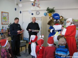 Dwóch policjantów, Mikołaj i Lupo rozdają upominki przedszkolakom