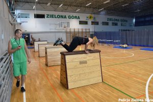 Kobieta w stroju sportowym skacząca przez skrzynię na sali gimnastycznej