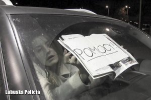 Kobieta jest zamknięta w samochodzie, trzyma w rękach kartkę z napisem &quot;POMOCY&quot;