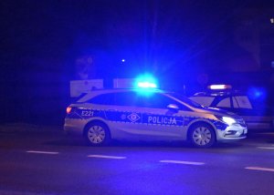 Srebrny radiowóz policji zielonogórskiej z włączoną sygnalizacją świetlną w nocy.
