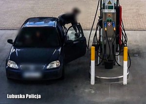 Granatowy samochód osobowy zaparkowany przy dystrybutorze paliwowym na stacji benzynowej.
