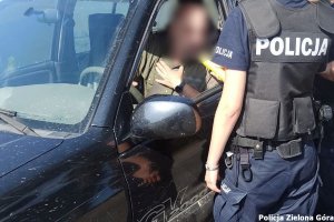 policjantka stojąca tyłem kontroluje trzeźwość kierującego siedzącego w czarnym samochodzie