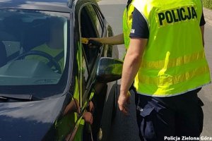 dwaj policjanci w żółtych odblaskowych kamizelkach kontrolują trzeźwość kierującego sierdzącego w granatowym samochodzie