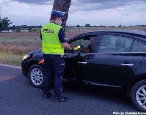 policjant w żółtej kamizelce odblaskowej sprawdza trzeźwość kierującego granatowym samochodem
