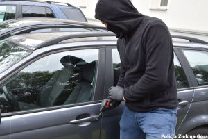 Zamaskowany mężczyzna próbuje otworzyć samochód śrubokrętem