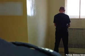 Mężczyzna stoi w celi policyjnego aresztu na tle zakratowanego okna