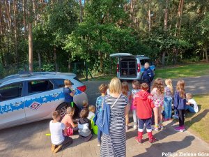 Policjant rozmawia z dziećmi, w tle dwa radiowozy policyjne