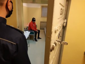 Policjant pilnuje  zatrzymanego mężczyznę siedzącego w celi